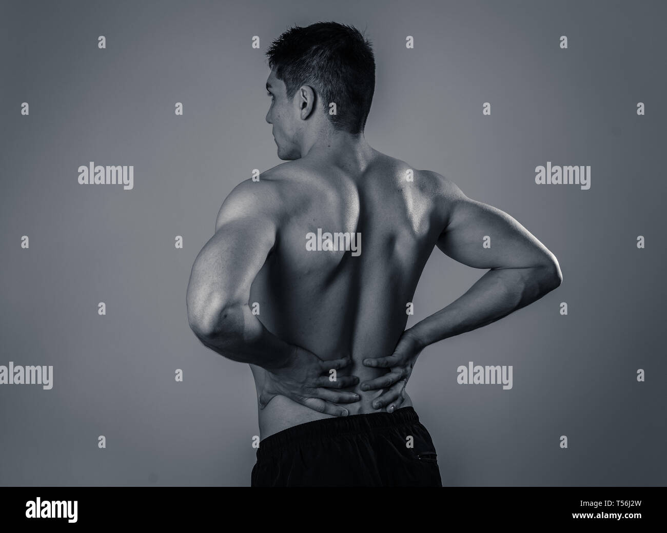 Jeune homme remise en forme musculaire touchant et saisissant son bas du dos souffrant de fortes douleurs après l'entraînement. Isolé sur fond neutre. Dans le sport un dommage je Banque D'Images