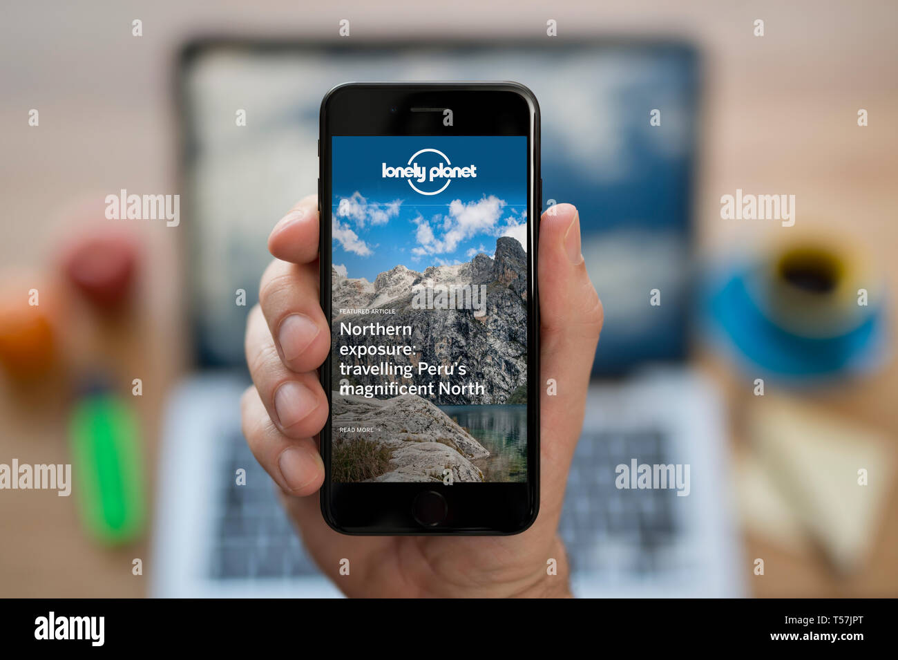 Un homme se penche sur son iPhone qui affiche le logo Lonely Planet (usage éditorial uniquement). Banque D'Images