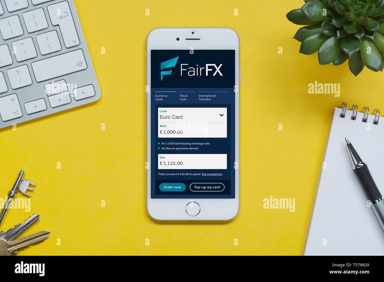 Un iPhone montrant le FairFX site repose sur un fond jaune table avec un clavier, les touches, le bloc-notes et des plantes (usage éditorial uniquement). Banque D'Images