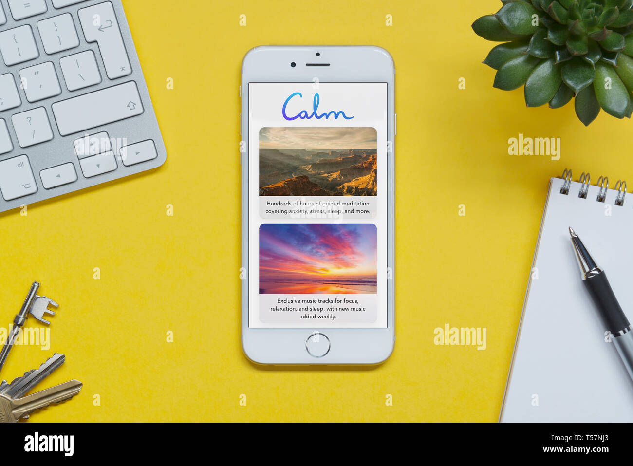 Un iPhone montrant le calme app repose sur un fond jaune table avec un clavier, les touches, le bloc-notes et des plantes (usage éditorial uniquement). Banque D'Images