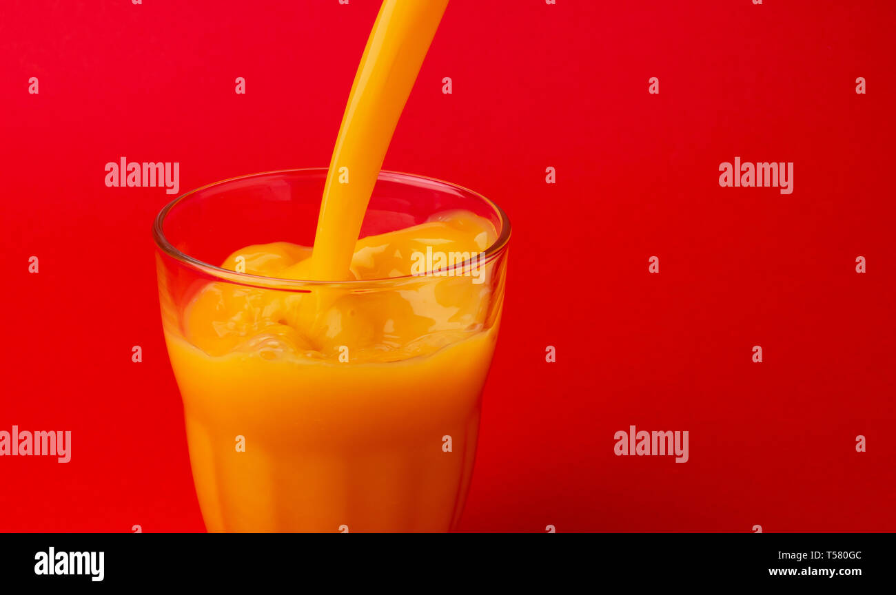 Le jus d'Orange et verser dans le verre, isolé sur fond rouge, avec copie espace Banque D'Images