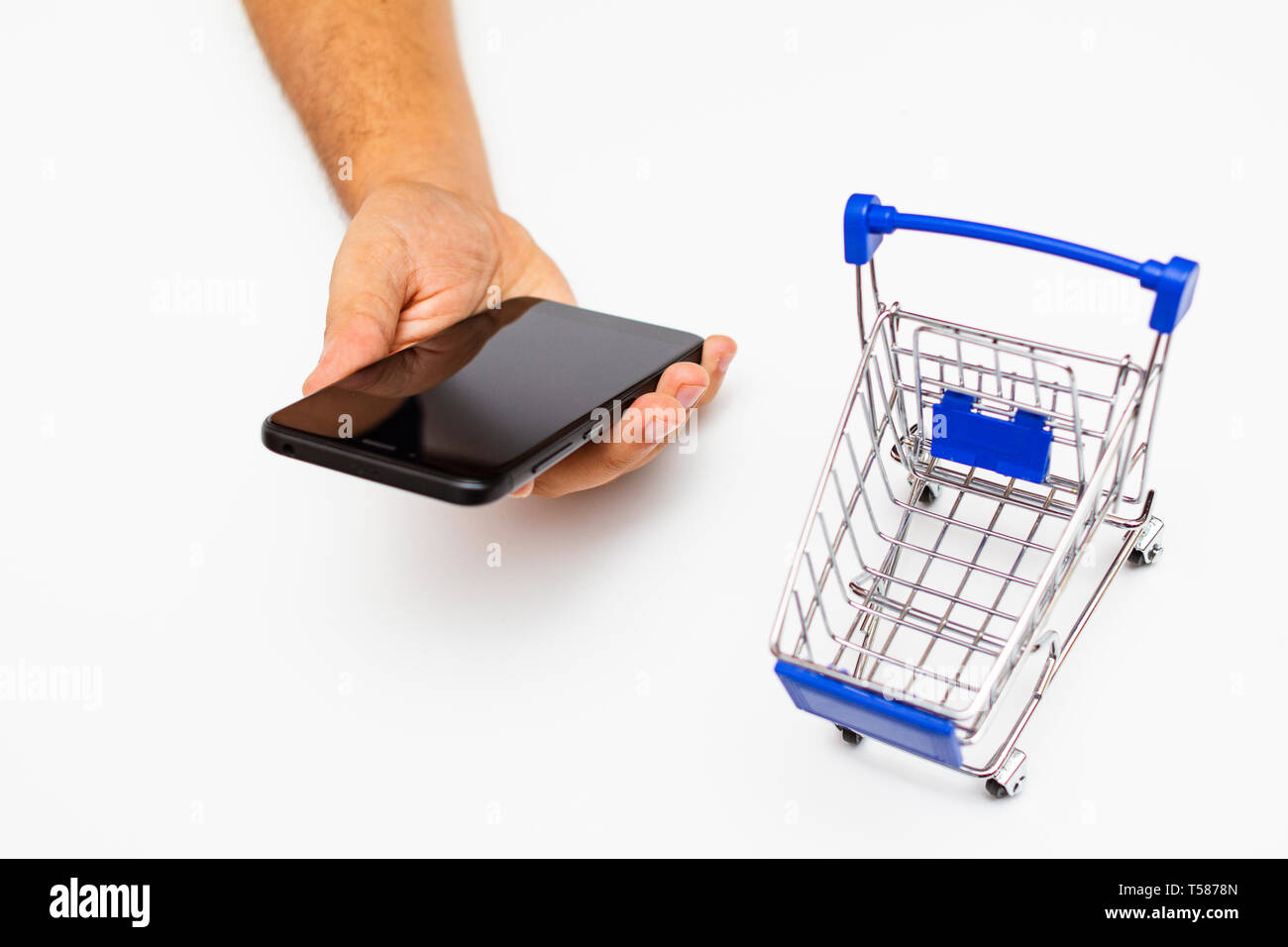 Portrait homme mains tenant un téléphone intelligent à côté d'un mini panier - online shopping concept Banque D'Images