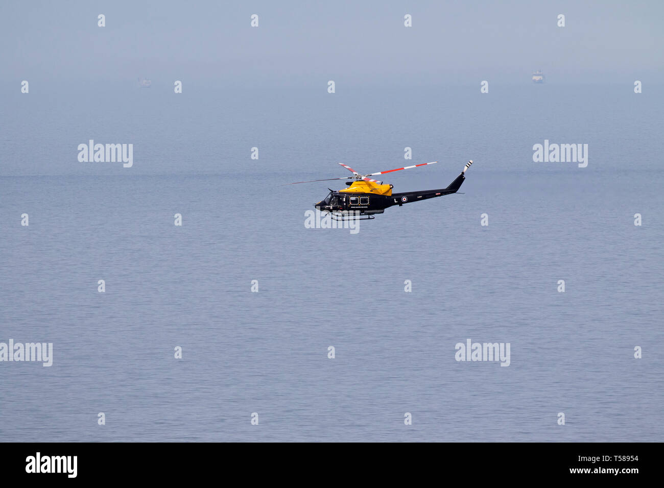 La défense de l'Hélicoptère Helicopter Flying School voler au-dessus de la mer au large des falaises de réserve RSPB South Stack Holyhead Anglesey Pays de Galles Royaume-uni le 2 avril Banque D'Images
