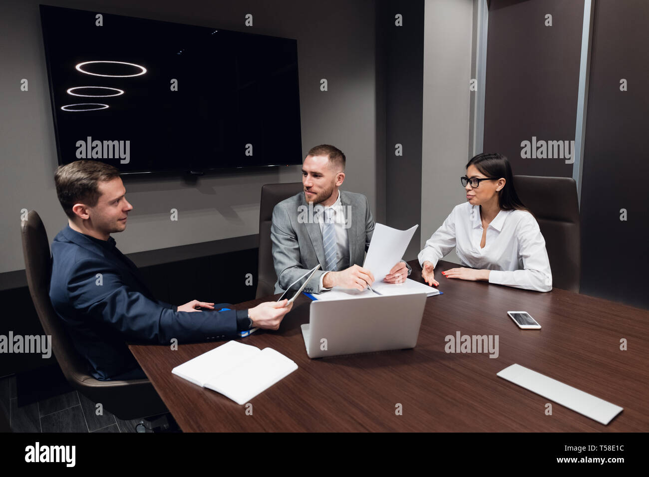 Jeune entreprise, l'entreprise créative des gens de différentes races et de l'âge se rassembler dans une salle de réunion dans l'intérieur de bureau moderne sombre, vivously à discuter Banque D'Images
