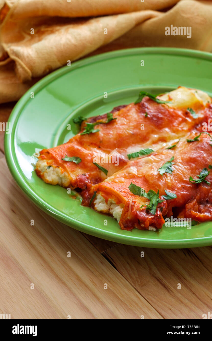 Plat de pâtes italiennes cuites au four farcies américain manicotti sur table de cuisine en bois Banque D'Images