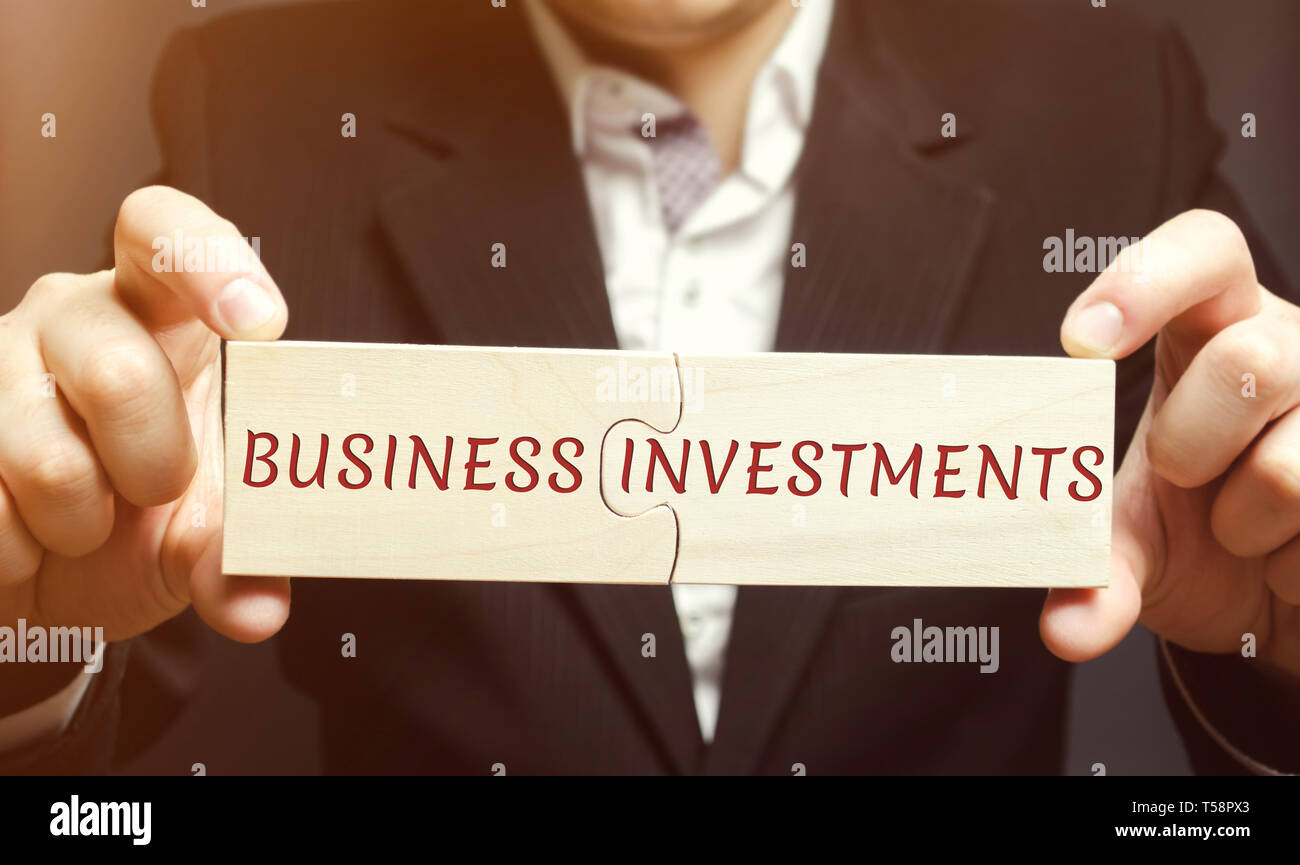 Businessman recueille des puzzles en bois avec les mots des investissements commerciaux. Augmenter le capital. Investir vos actifs dans votre propre ou celle de quelqu'un d'entreprise Banque D'Images