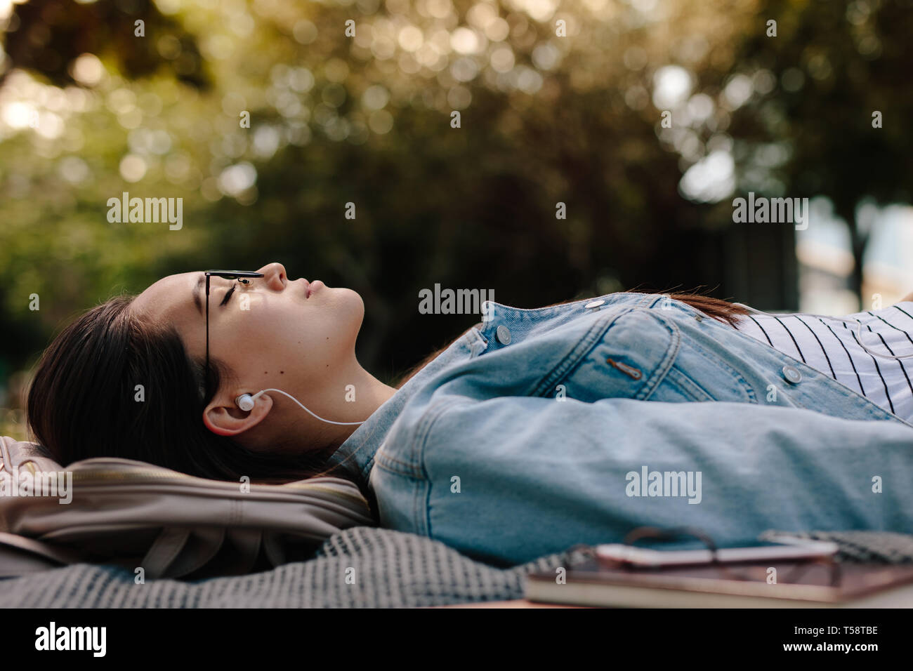 Gros plan d'une femme dormant dans un parc à l'écoute de musique. Niveau du sol tourné d'une jeune femme étendue sur le sol portant des lunettes avec des livres à côté d'elle Banque D'Images