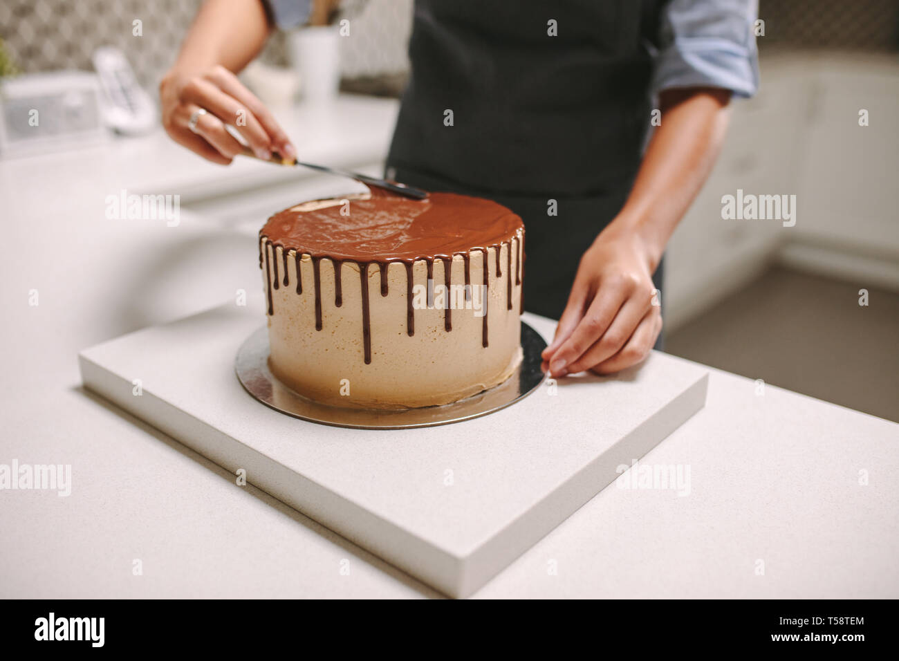 Chef pâtissier la préparation d'un gâteau dans la cuisine. Confiseur chocolat femelle répand le glaçage sur un gâteau. Banque D'Images