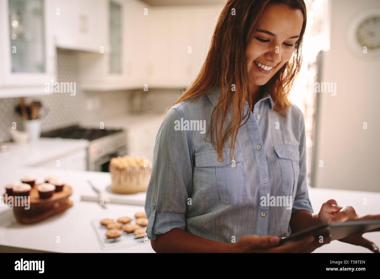Chef pâtissier using digital tablet in cuisine. Confiseur femelle tablet avec parties sur comptoir de la cuisine à l'arrière. Banque D'Images
