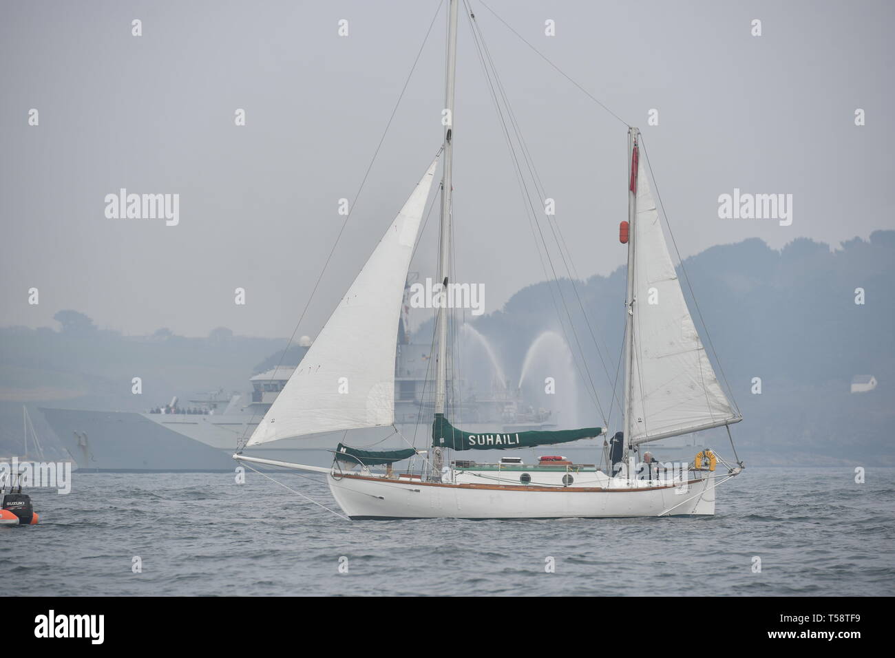 Sir Robin Knox-Johnson à bord Suhali, passant d'un navire de guerre de la marine royale comme il vient de franchir la ligne d'arrivée de son premier voyage à Falmouth, à l'occasion du 50e anniversaire de son achèvement de la première circumnavigation sans escale du monde. Banque D'Images