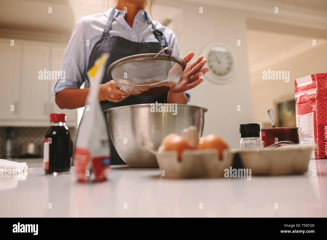 Chef sasser la farine dans un bol pour faire un gâteau au chocolat. Femme portant un tablier la cuisson dans la cuisine avec des ingrédients autour. Banque D'Images