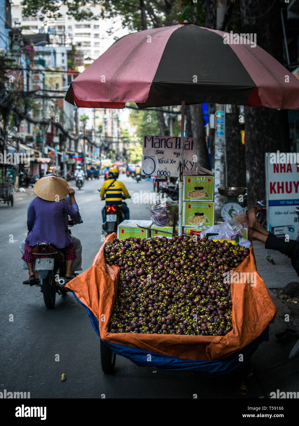 Stand de la route avec le panier plein de fruits mangoustan et les motos qui passent, Ho Chi Minh City, Vietnam, Asie Banque D'Images