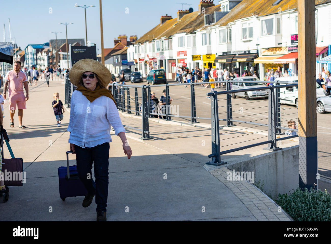 Les femmes d'âge moyen portant un grand chapeau d'été tirant un sac shopping le long de la promenade de Littlehampton Banque D'Images