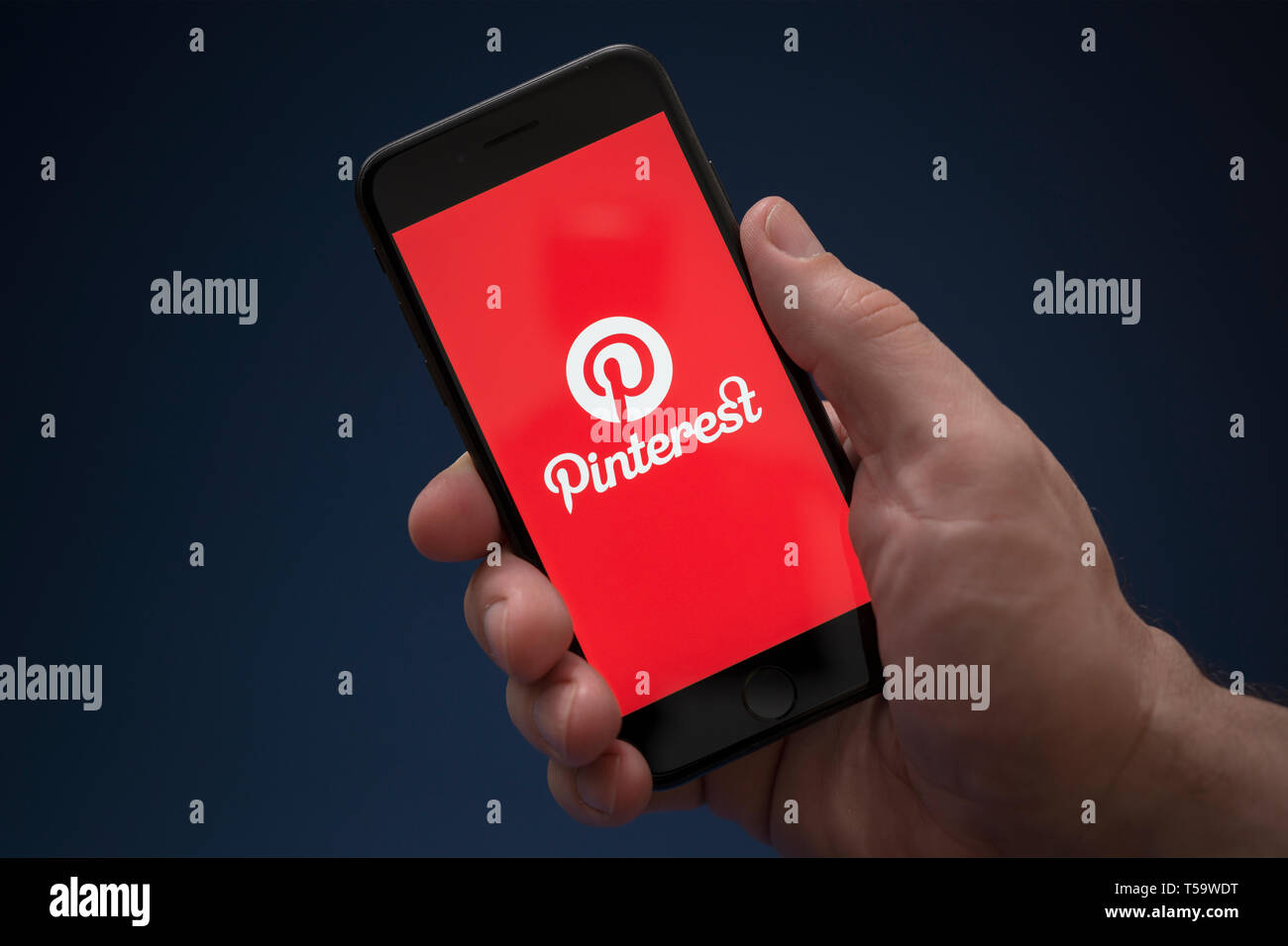 Un homme se penche sur son iPhone qui affiche le logo Pinterest (usage éditorial uniquement). Banque D'Images