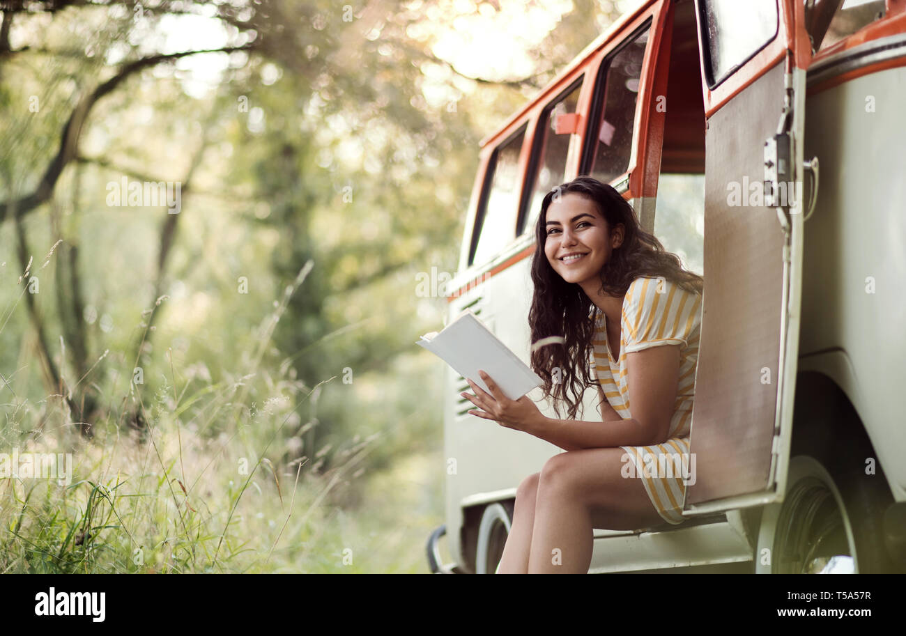 Une jeune fille avec réserve par une voiture sur un roadtrip à travers campagne, lecture. Copier l'espace. Banque D'Images