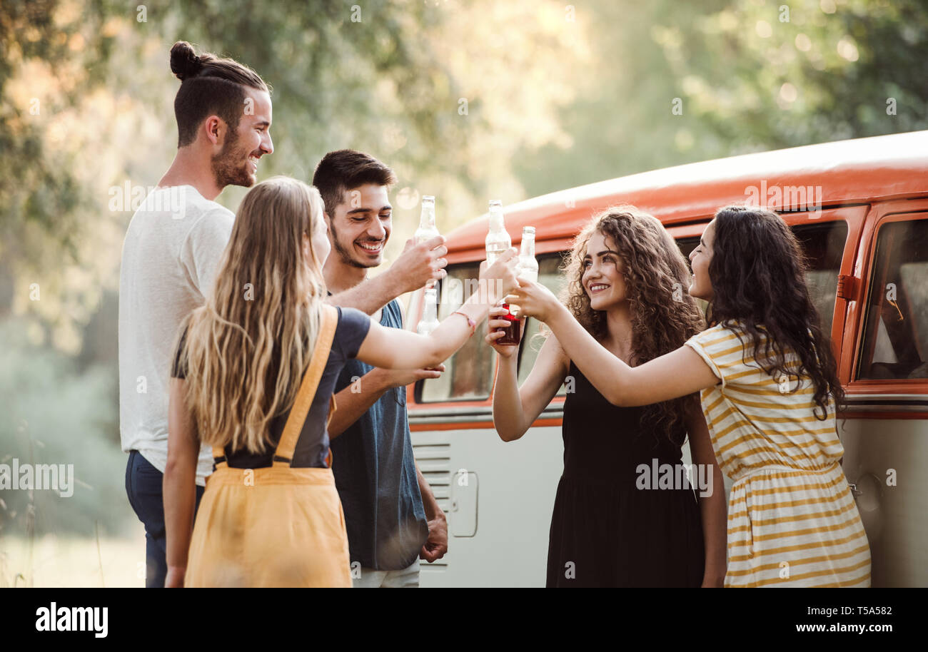 Un groupe de jeunes amis avec des boissons en plein air permanent sur un roadtrip à travers campagne, tintement des bouteilles. Banque D'Images