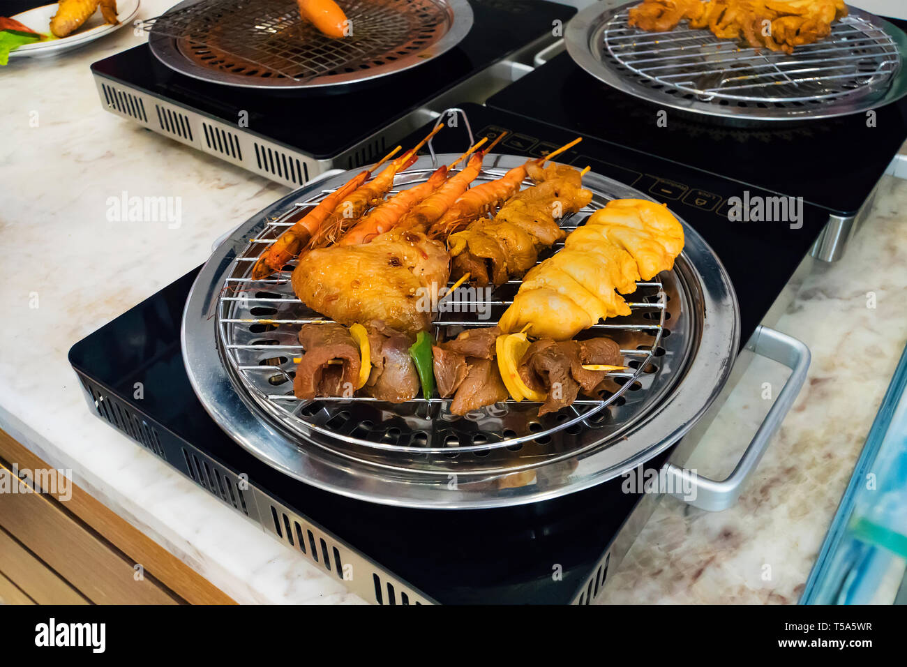 Différents types de kebabs sont frits sur un gril électrique dans la cuisine du restaurant de l'hôtel. La cuisson à la maison. Poêlée de crevettes, poulet, boeuf, porc frie Banque D'Images