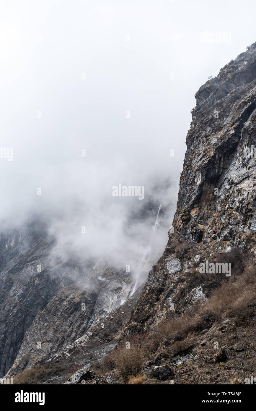 Falaise de montagne brumeuse avec chute d'eau sur la route de trekking dans le circuit Annapurna. Népal Banque D'Images