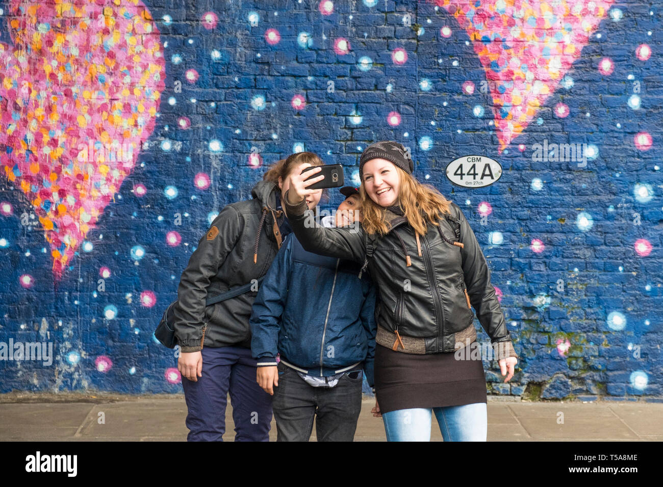 Amis posant pour un selfie devant une grande murale peinte de cœurs roses peints par Jimmy C à la mémoire des attaques terroristes du London Bridge. Banque D'Images