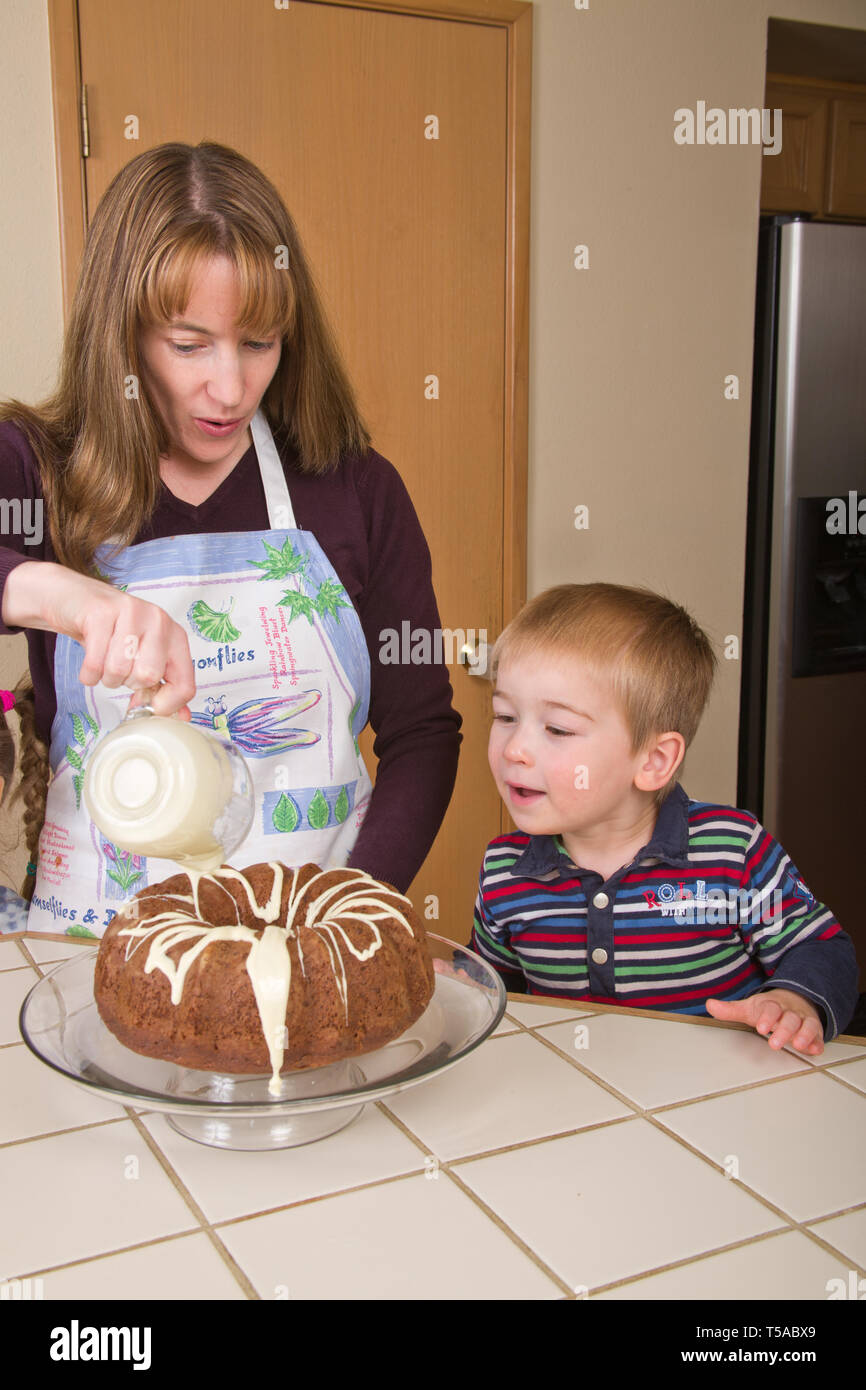 Verser le glaçage au chocolat blanc mère sur gâteau bundt chocolat tout en fils de trois ans montres. (MR) Banque D'Images