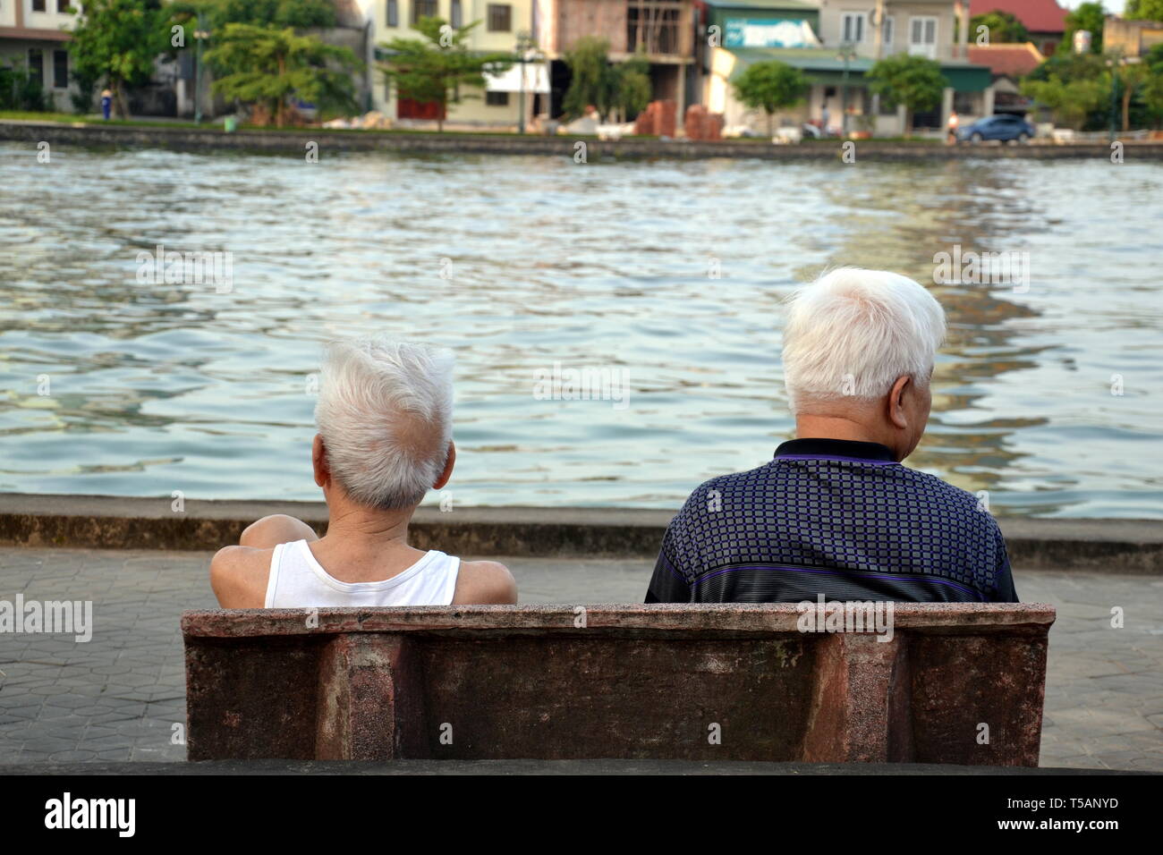 Vue arrière des deux hommes âgés assis sur un banc avec vue sur un lac en Ha Tinh, au Vietnam, en mai 2017. Banque D'Images