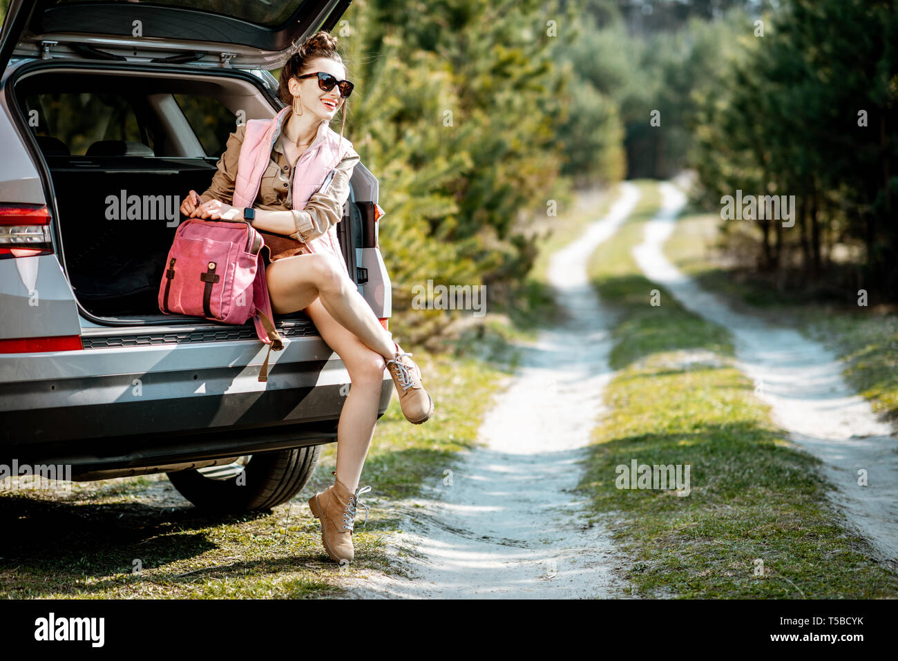 Jeune femme profiter de la nature tout en restant assis dans le coffre de la voiture sur une route pittoresque dans les bois Banque D'Images