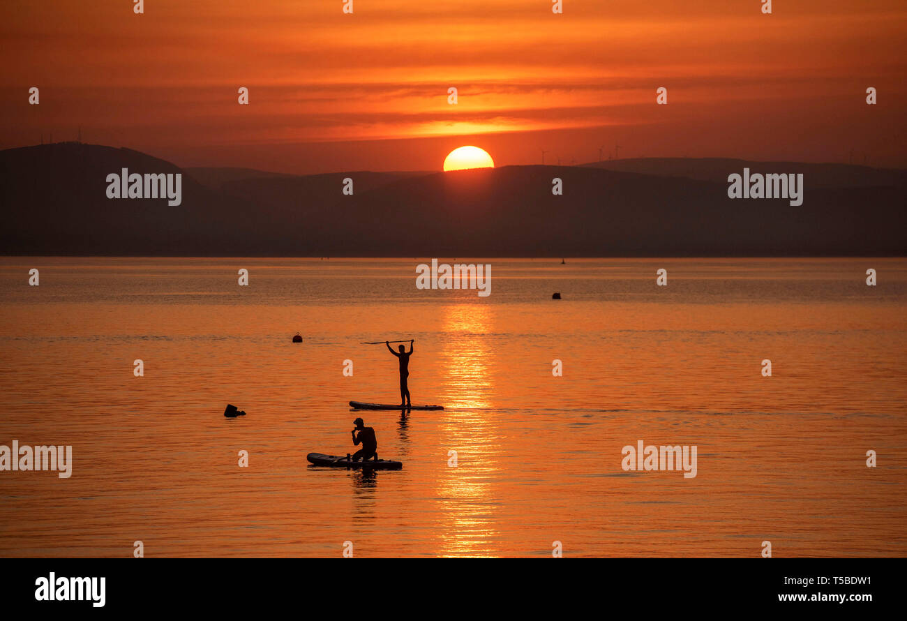 Un paddleboarder prend une photo de son ami pendant la semaine de Pâques magnifique lever du soleil près du petit village de Mumbles près de Swansea ce matin en tant que Banque D'Images