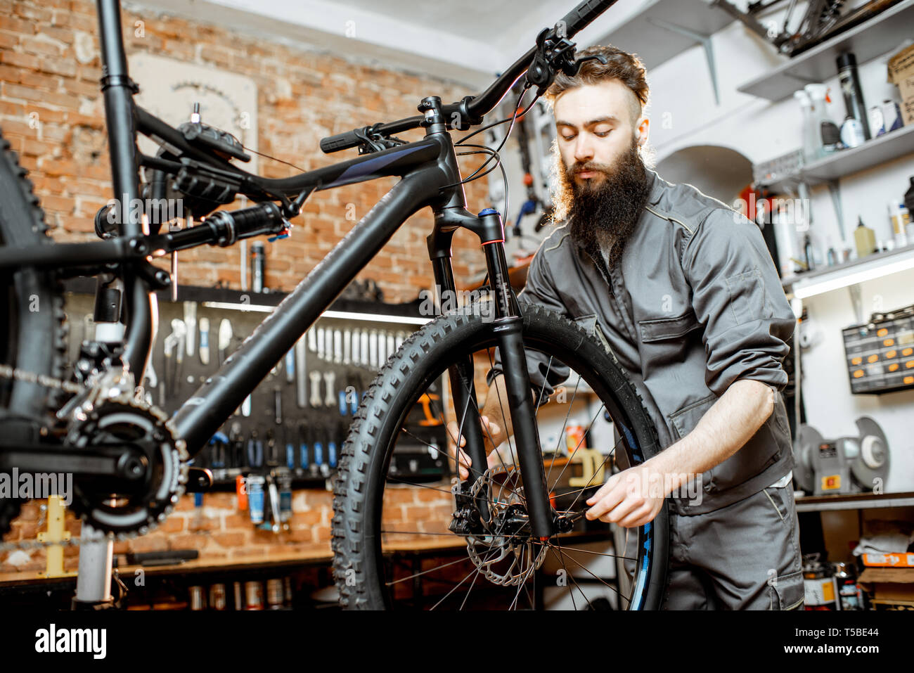 Beau réparateur à barbu de vêtements de roue d'un vélo de montagne à l'atelier Banque D'Images