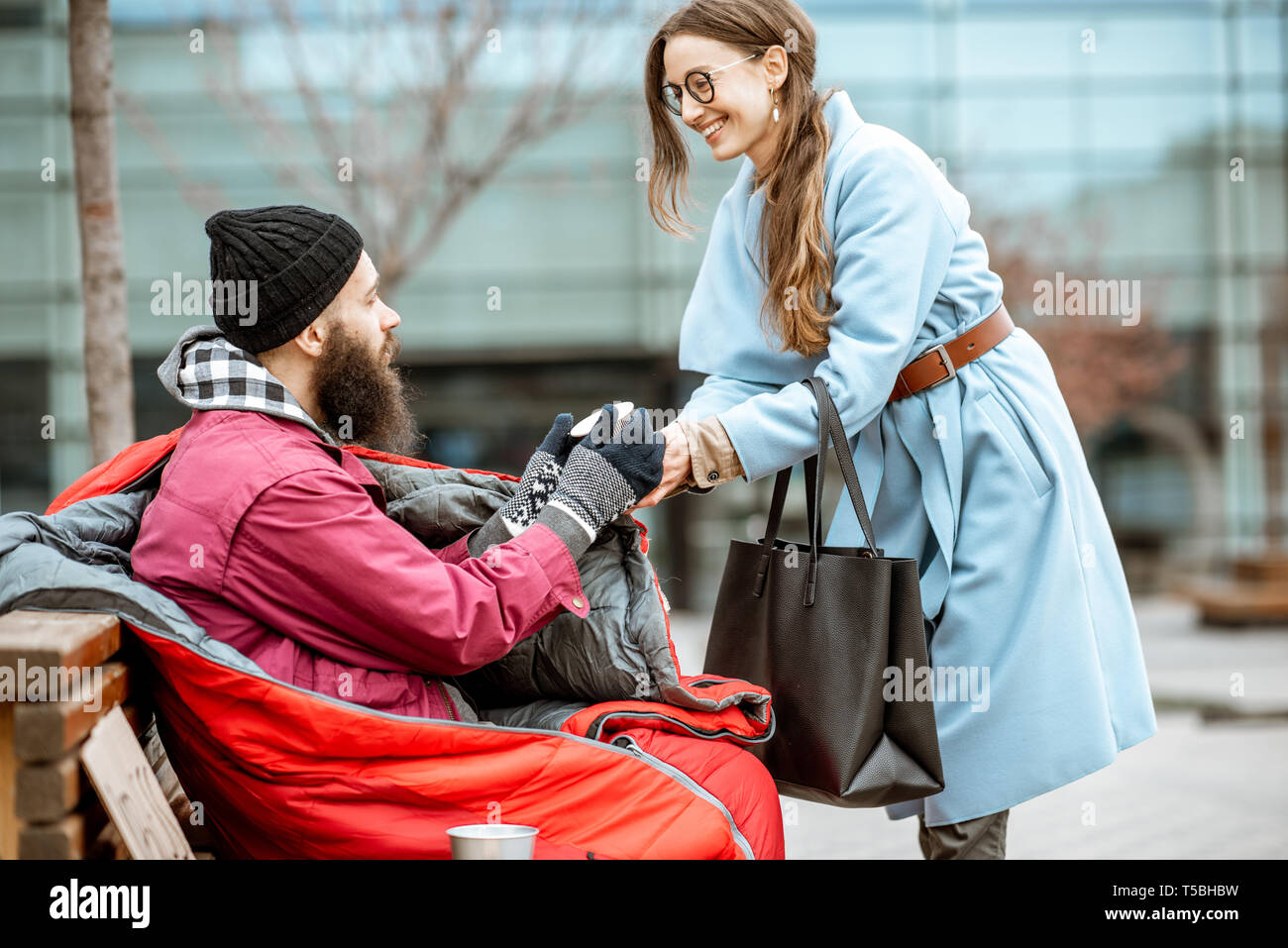 Femme d'aider les sans-abri mendiant donnant une boisson chaude à l'extérieur. Concept d'aider les pauvres Banque D'Images