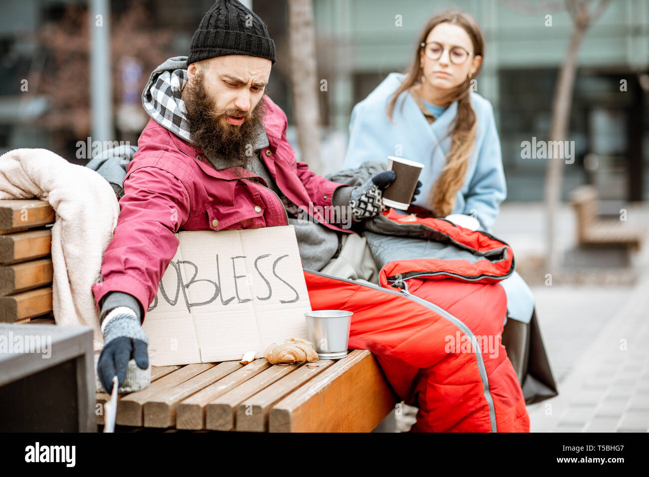 Jeune femme aide à un sans-abri mendiant assis sur le banc à l'extérieur. Concept d'un accord entre le pauvre et le riche Banque D'Images