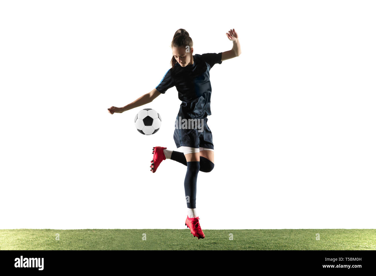 Jeune joueur de football ou de soccer féminin aux cheveux longs en sportwear et chaussures coups de balle pour l'objectif dans les sauts isolé sur fond blanc. Concept de vie sain, le sport professionnel, passe-temps. Banque D'Images