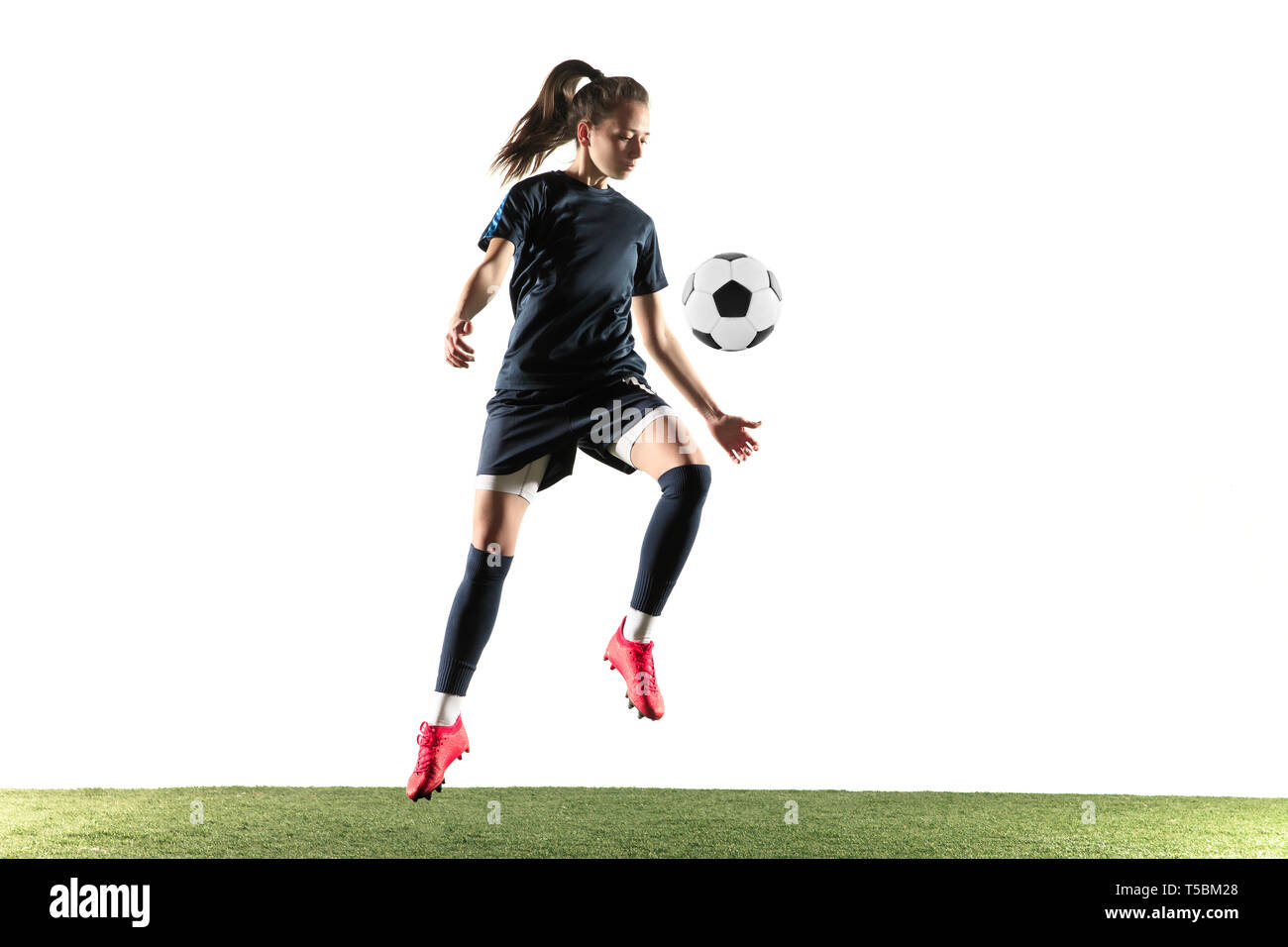 Jeune joueur de soccer ou de football féminin aux cheveux longs en sportwear et chaussures coups de balle pour l'objectif dans les sauts isolé sur fond blanc. Concept de vie sain, le sport professionnel, passe-temps. Banque D'Images