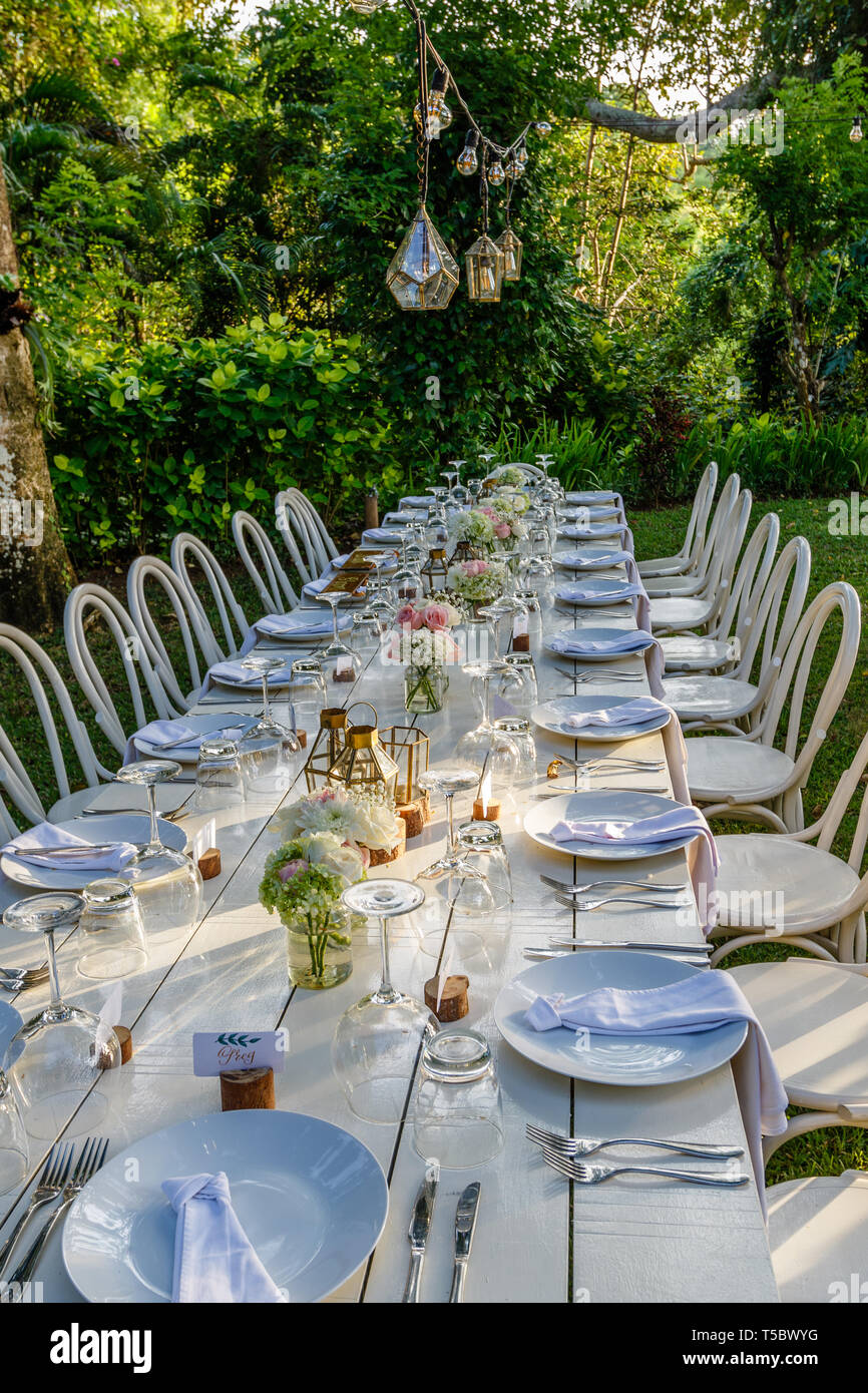 Set Table pour un dîner de mariage décoré avec des bouquets de rose et verre. Chaises en bois blanc. Étiquettes de nom de calligraphie. Mariage Tropical. Banque D'Images