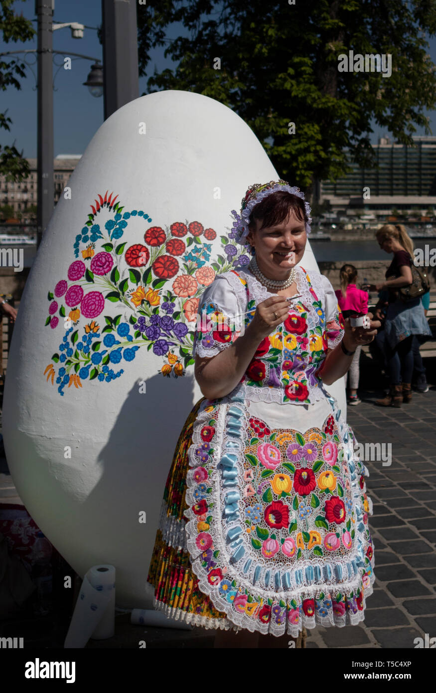 BUDAPEST/Hongrie - 04.21.2019 : une femme en costume traditionnel folk brodé décore un Œuf de Pâques géant avec des motifs floraux. Banque D'Images