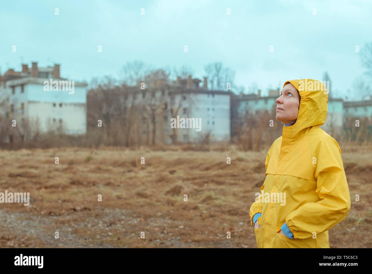 Femme en imperméable jaune jusqu'à la pluie alors que les nuages en gouttes tombent sur son visage Banque D'Images