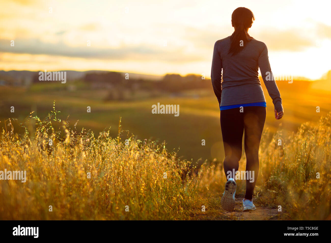 Jeune femme énergique du jogging à travers le paysage rural au coucher du soleil. Banque D'Images