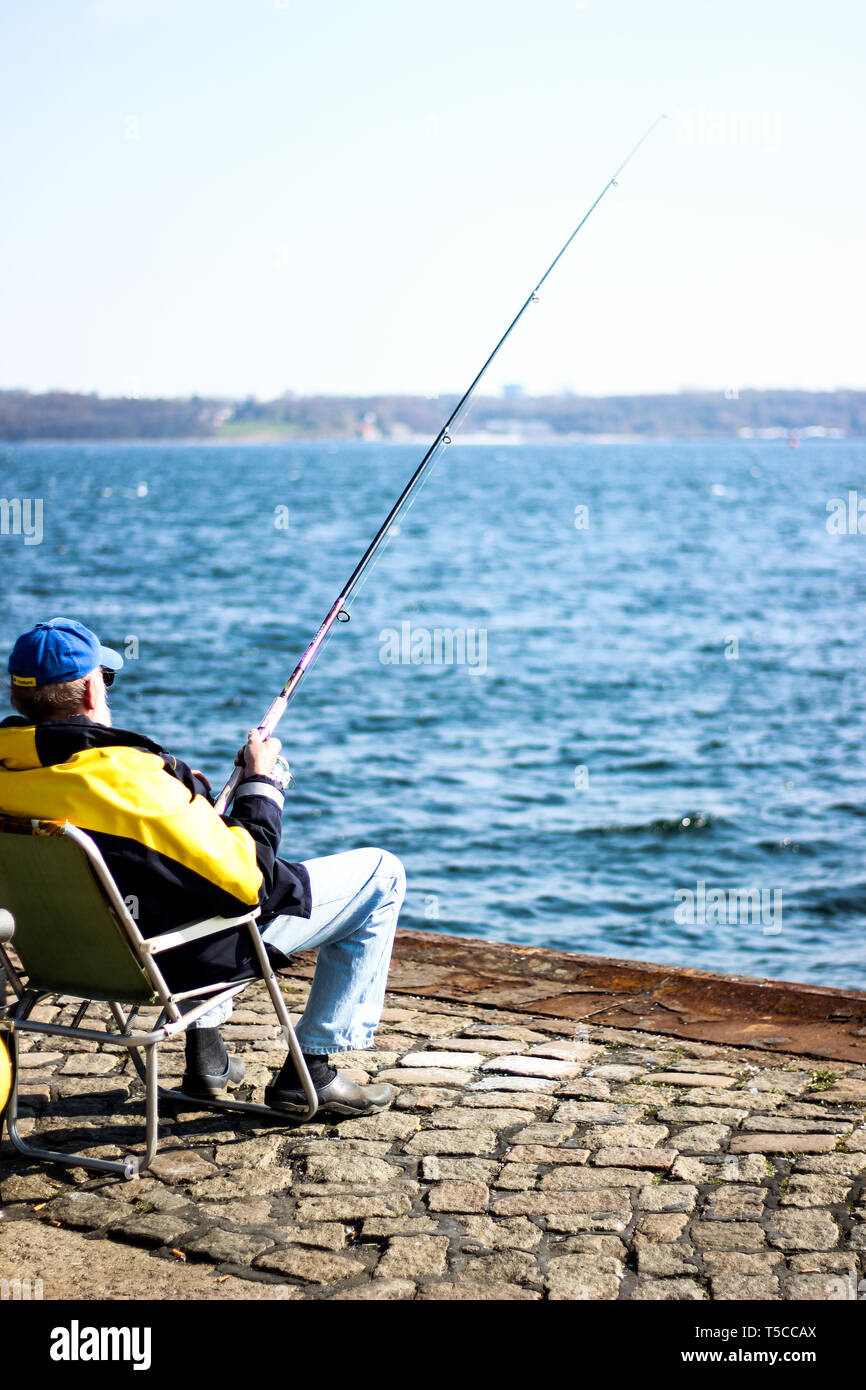 Dans Fischersmann schwarz-gelber Jacke sitzt Kieler Förde un ange mit und fängt Fische Banque D'Images