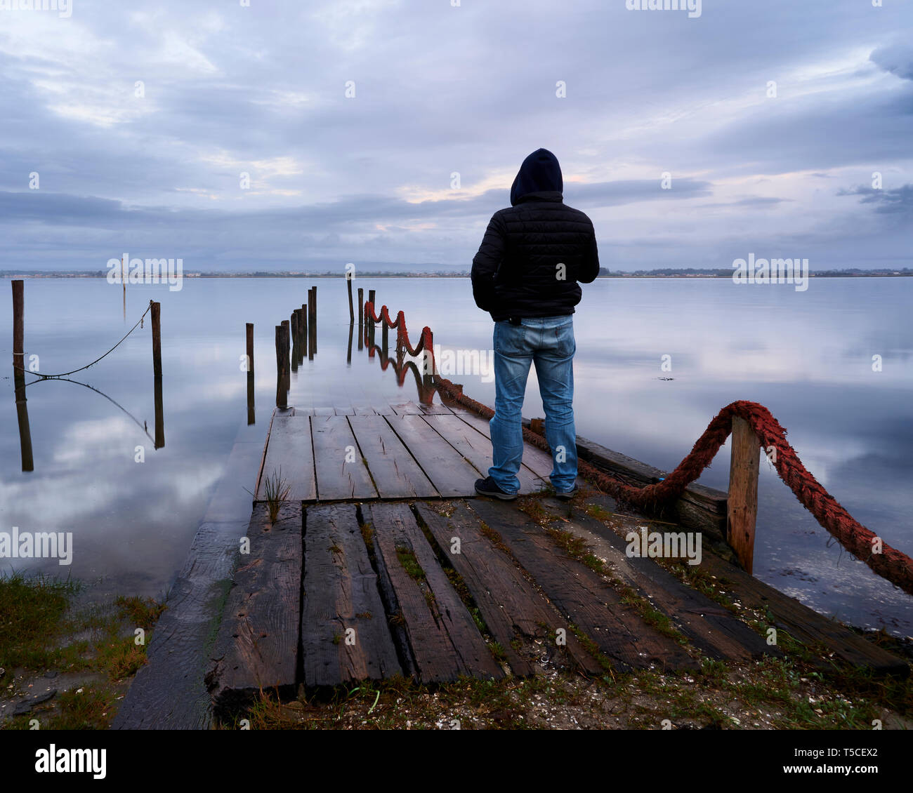 Homme debout dans l'entrée de l'palafitic pier submergé par la marée haute à la fin de la journée, seuls les Polonais sont visibles. Blue Hour witna teinte d'orang Banque D'Images