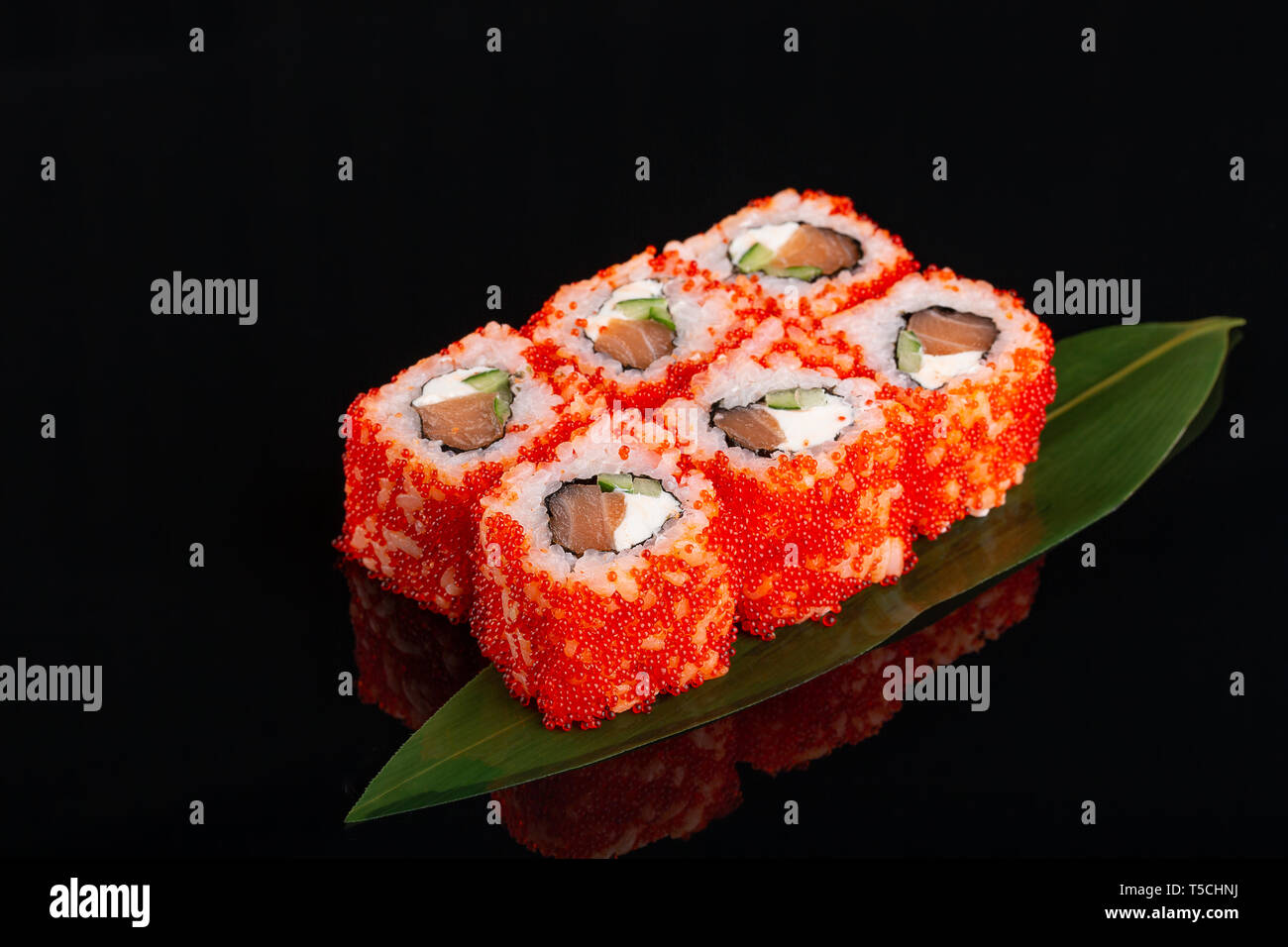 Rouleau de Philadelphie Uramaki rempli de saumon, concombre, avocat et fromage à la crème. Rouleaux Philly recouvert d'oeufs de poisson volant rouge sur feuille de bananier à blac Banque D'Images