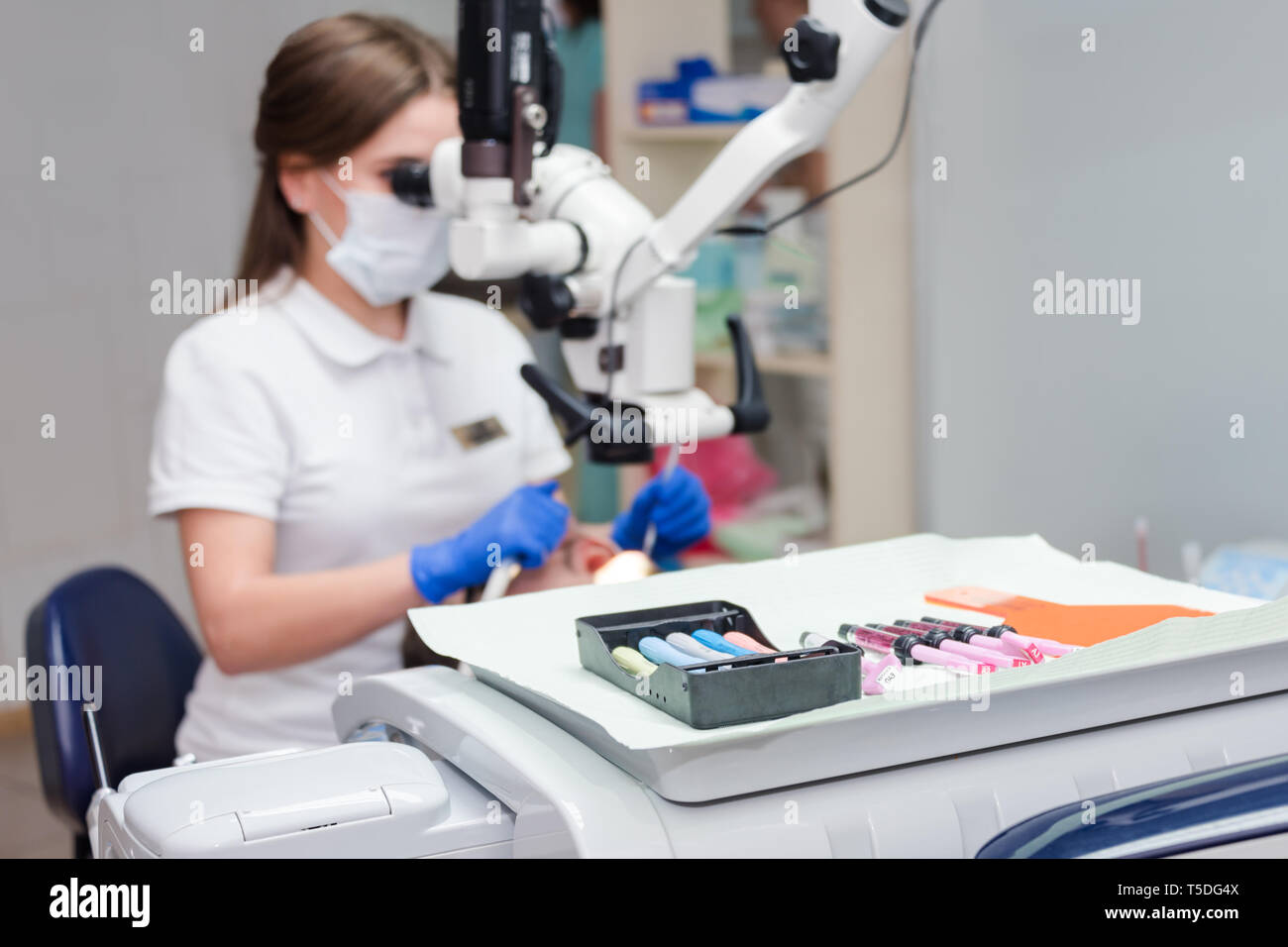 Jeune femme dentiste traitant des traitements de canaux à l'aide de microscope optique à la clinique dentaire. Jeune homme patient couché sur le fauteuil du dentiste avec la bouche ouverte. Dentiste Banque D'Images