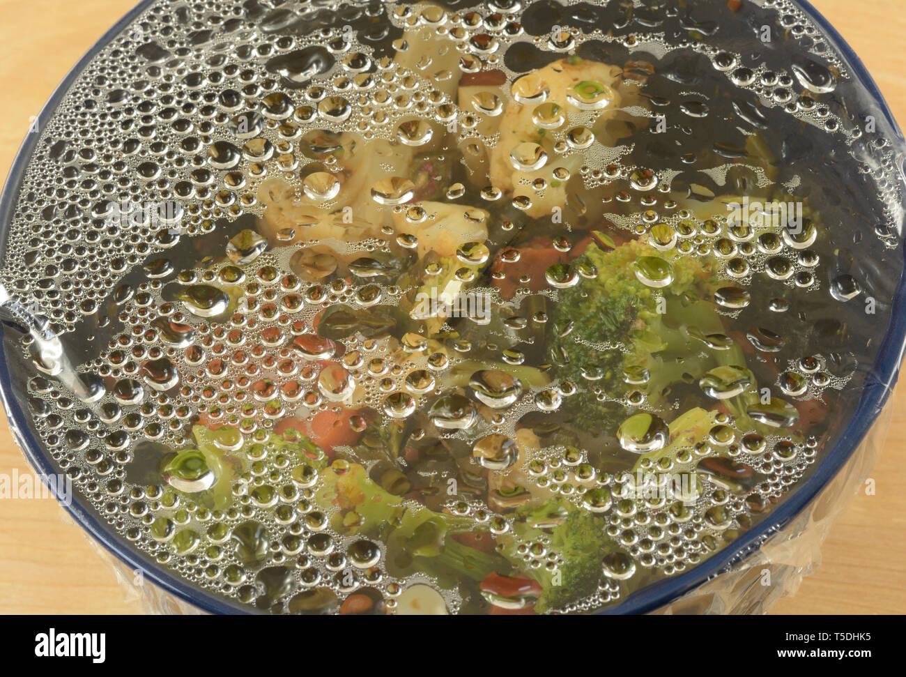 La condensation d'eau sur une pellicule plastique sur le bol de restes de légumes pris hors du réfrigérateur pour réchauffer le dîner Banque D'Images