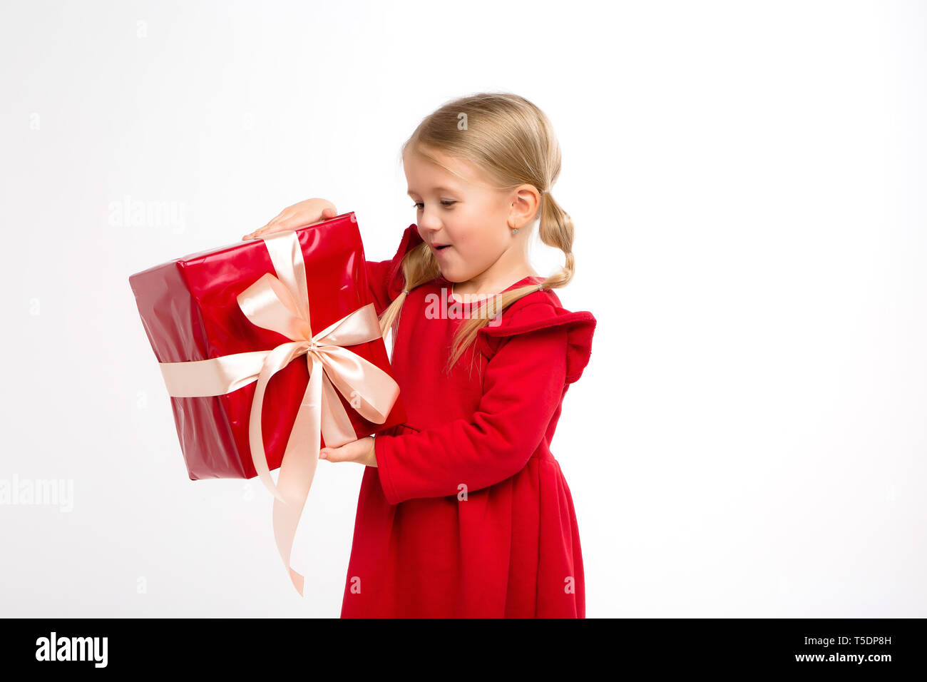 Portrait de petite fille en robe rouge isolé sur fond blanc. Smiling Girl in shirt avec cadeaux dans les mains à la recherche à l'appareil photo. Gris isolé backgrou Banque D'Images