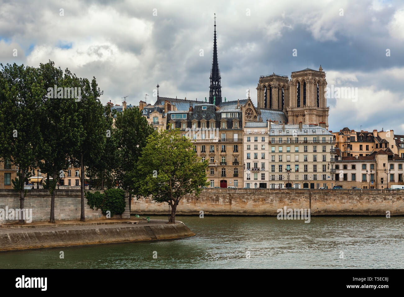 Vue sur Seine et flèche de la cathédrale Notre-Dame de Paris célèbre parmi les immeubles parisiens typiques sous ciel nuageux. Banque D'Images