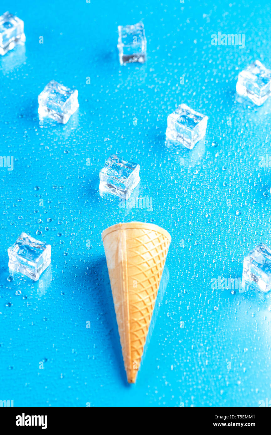 Cornet de crème glacée vide et des cubes de glace sur fond bleu Banque D'Images