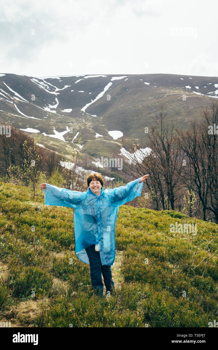 Happy smiling senior voyageur belle femme en bleu veste de pluie et un jean dans les montagnes, entourée de forêt, profiter du silence et l'harmonie de la nature Banque D'Images