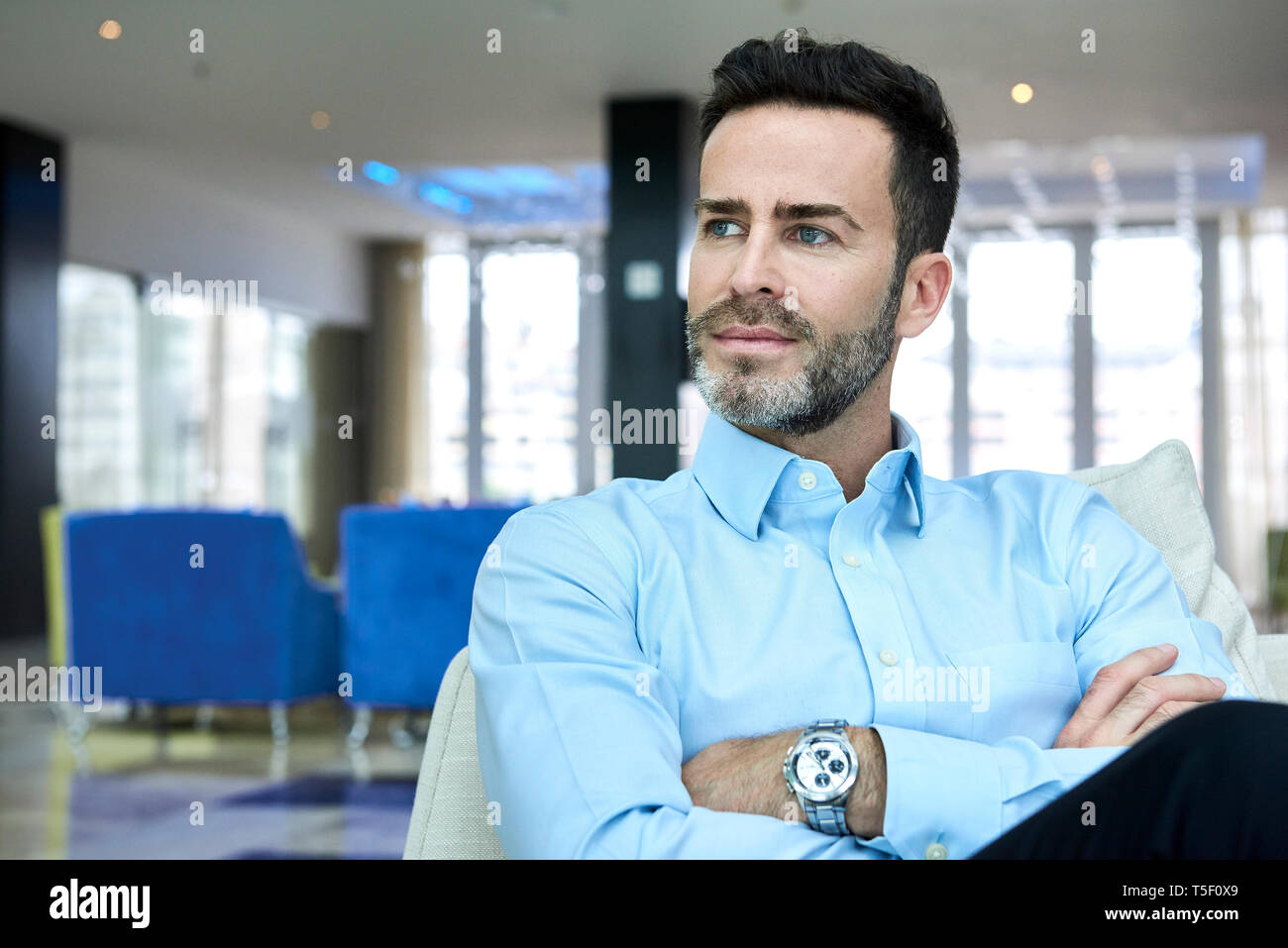 Businessman sitting on sofa with arms crossed Banque D'Images