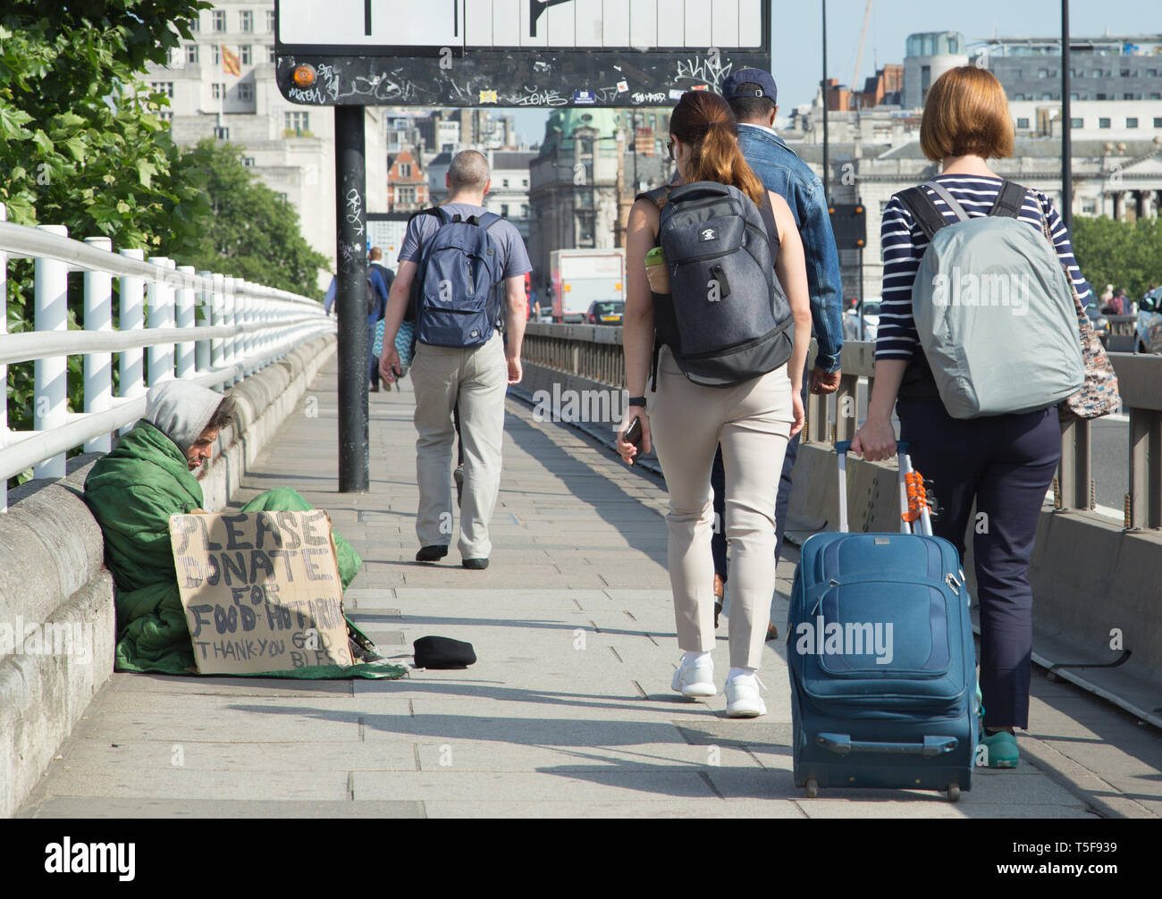 Apparemment, un homme sans foyer avec un carton à la main pour l'alimentation sur demande inscription Waterloo Bridge à Londres avec les navetteurs et les voyageurs passant par Banque D'Images