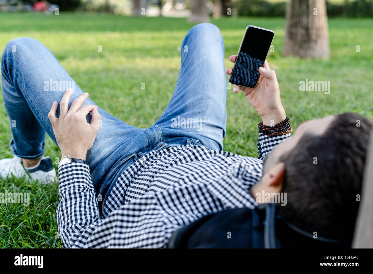 Man lying on meadow in city park using smartphone Banque D'Images