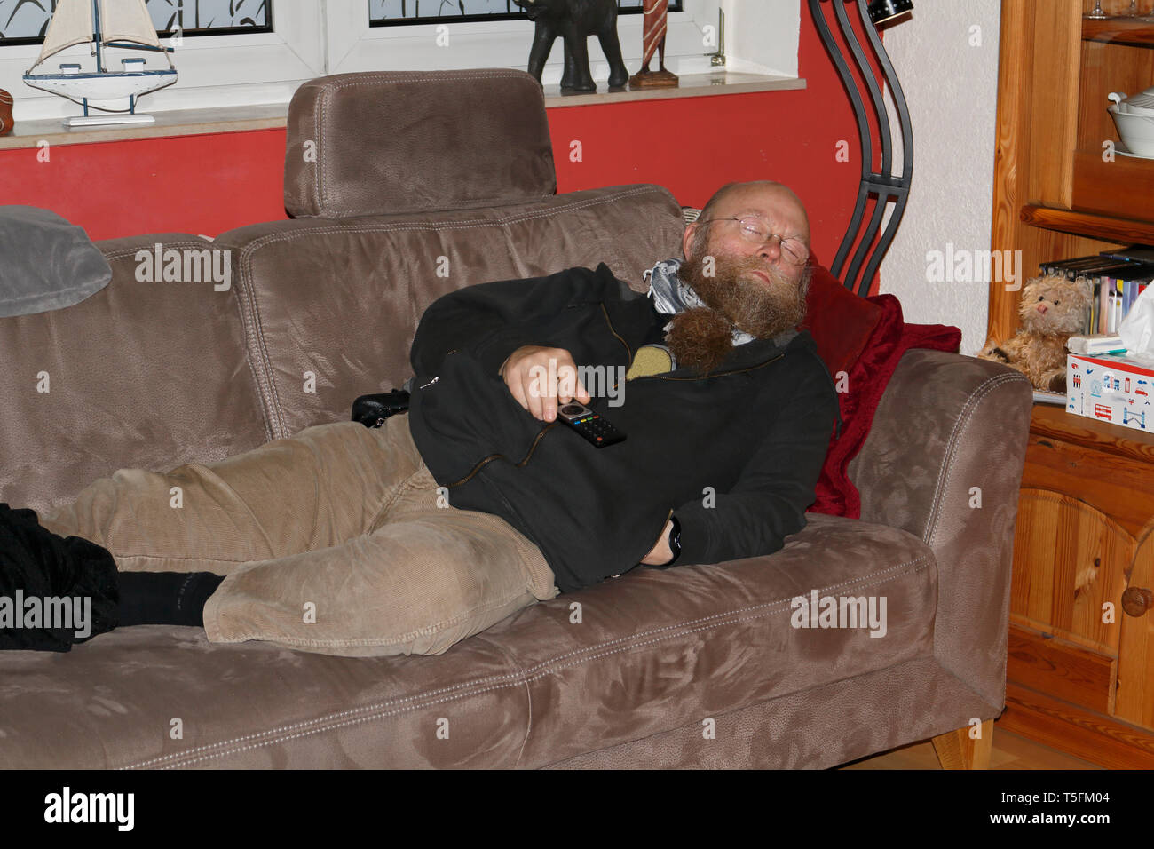 Mann mit langem Bart, mit der Fernbedienung in der Hand, ist auf der Couch eingeschlafen Banque D'Images
