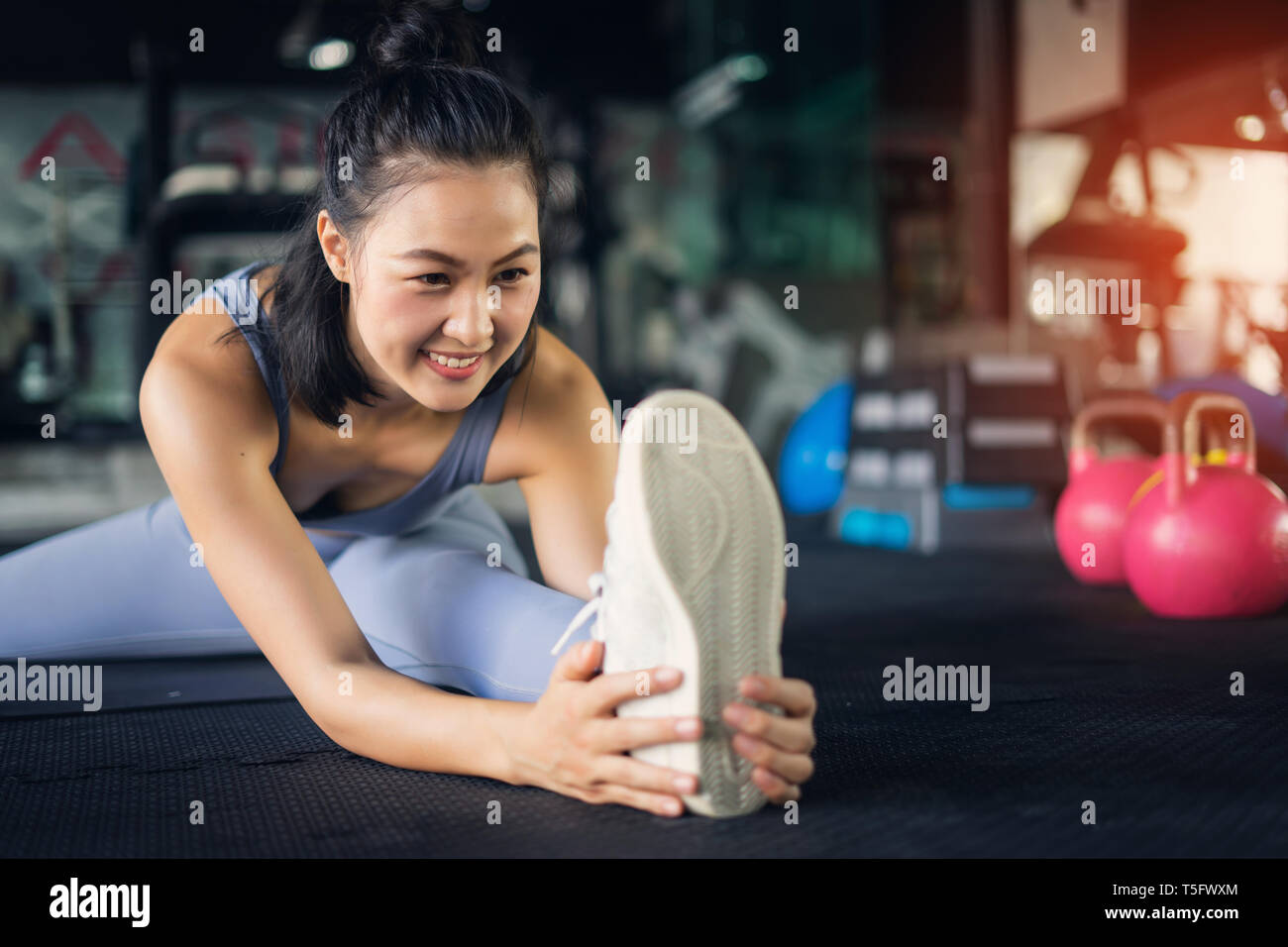 Young Asian Woman in healthy lifestyle assis sur un tapis de yoga étirement pied holding jambe. l'exercice et de remise en forme santé concept dans une salle de sport. Banque D'Images
